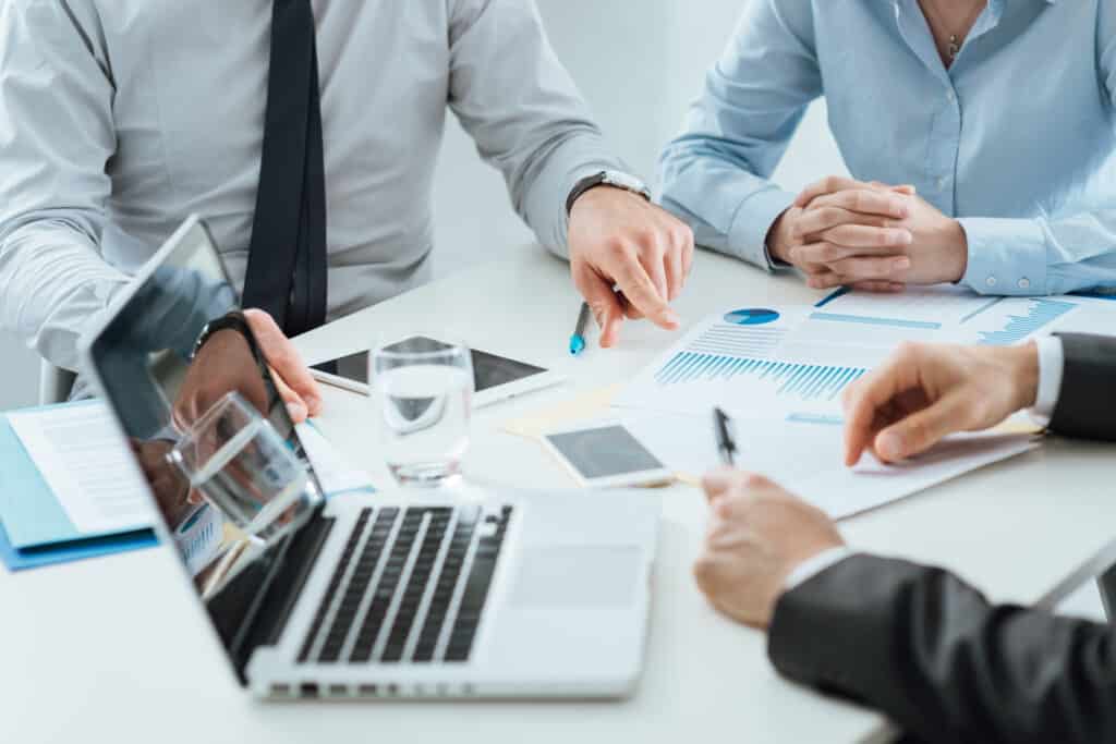 Business professionals collaborating over documents and a laptop, discussing strategies and analytics for IT services in a modern office setting.