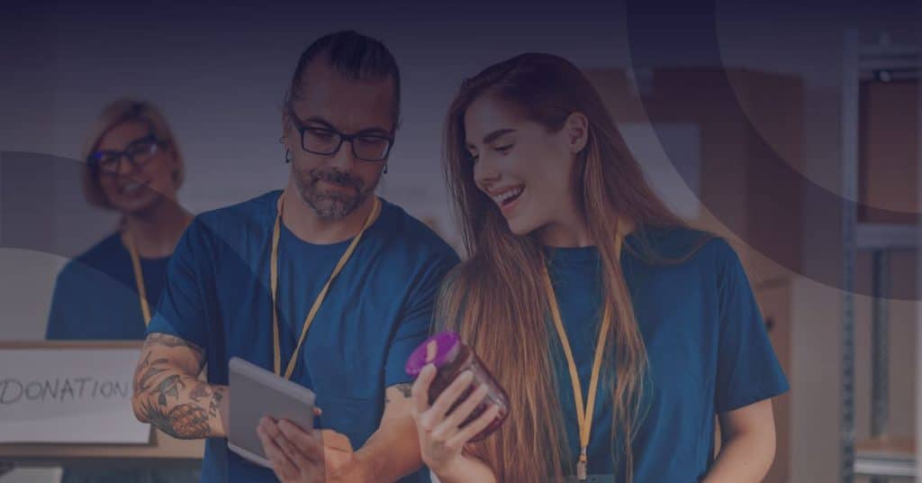 Volunteers collaborating in a non-profit setting, examining a donation jar and tablet, emphasizing digital transformation and community engagement in the charity sector.