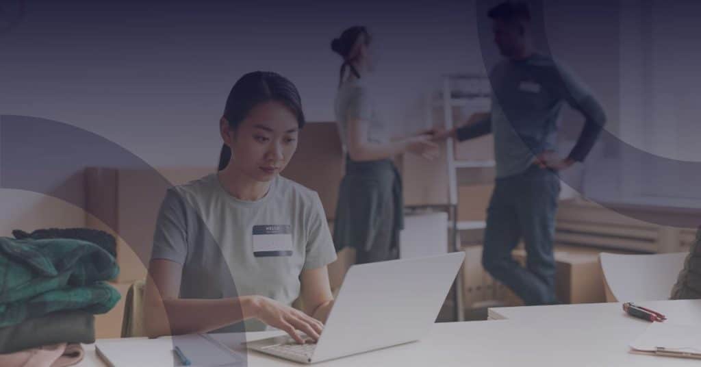 Woman working on a laptop in a not-for-profit organization, collaborating with team members in a supportive environment, emphasizing the need for cost-effective IT solutions.