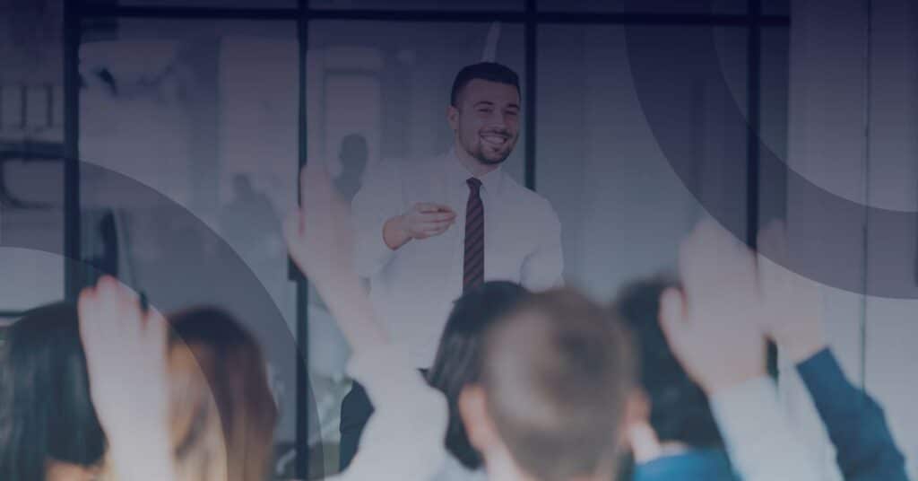 Business professional leading a security awareness training session with engaged audience raising hands, emphasizing the importance of cybersecurity education.