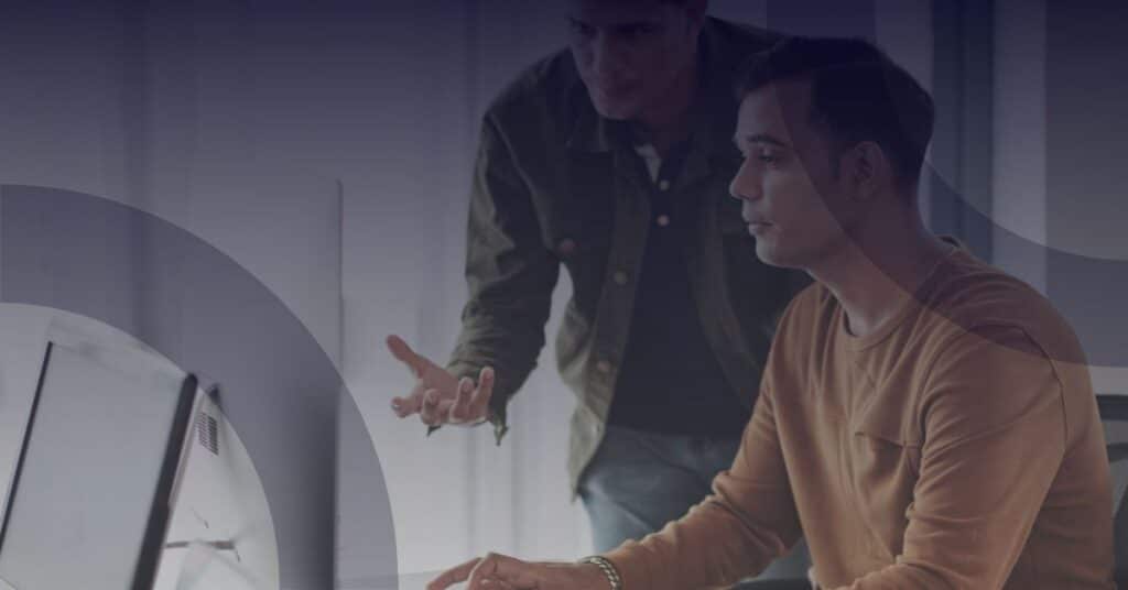 Two men discussing IT issues at a computer, highlighting collaboration in addressing resource challenges faced by not-for-profit organizations.