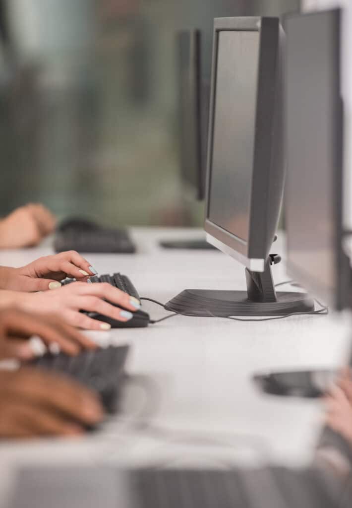 Hands typing on keyboards in a modern office setting with multiple computer monitors, illustrating managed IT services and collaborative work environments.