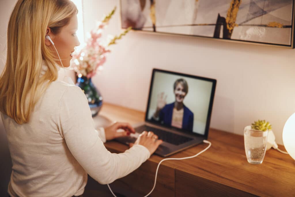 Woman using laptop for video call with Microsoft Teams, featuring earphones and a modern workspace setup.