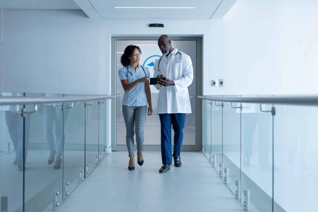 Diverse male and female healthcare professionals walking in a modern hospital corridor, discussing patient care and technology solutions in a public sector context.