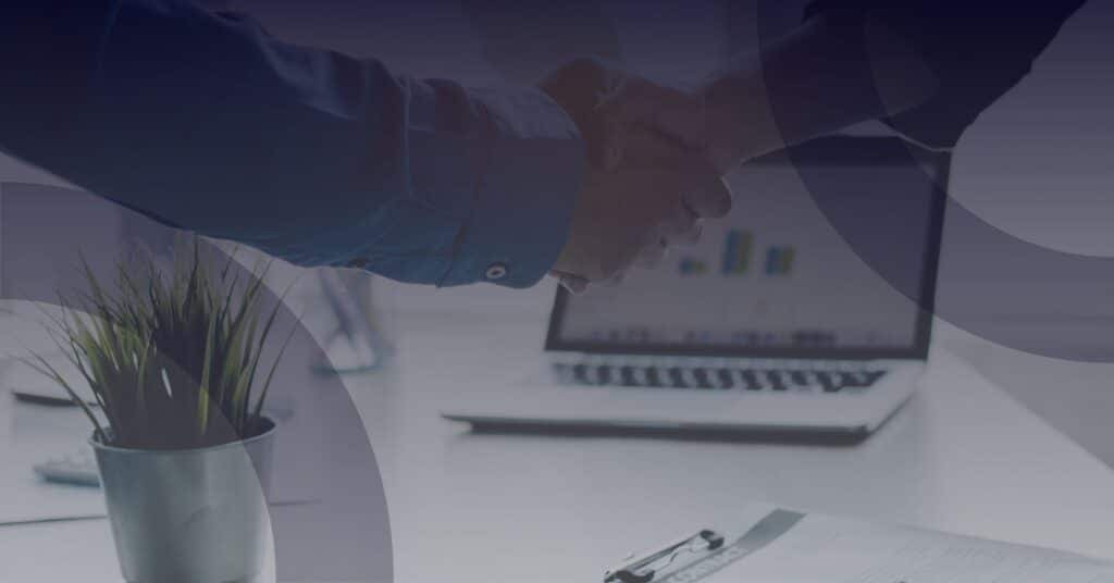 Hands shaking in a business setting, symbolizing partnership, with a laptop and documents in the background, representing Reliable Networks' managed Microsoft 365 services.