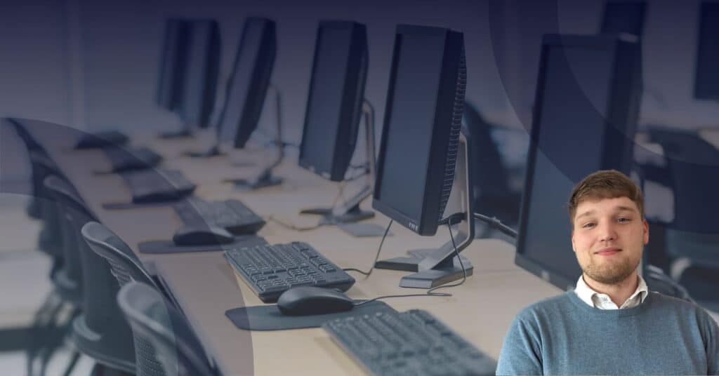 Person in a blue sweater standing in front of a row of desktop computers, illustrating the importance of managed IT services for businesses.