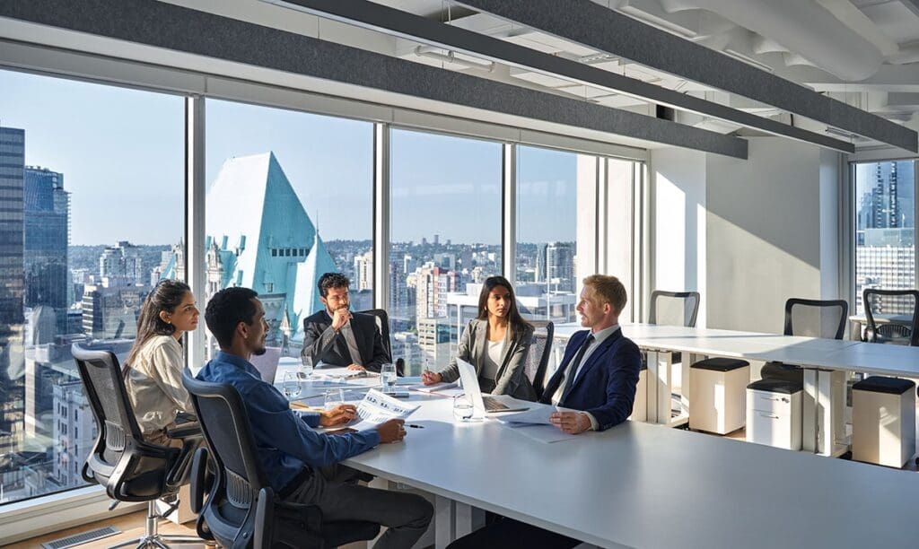 Diverse team of executives in a modern office meeting, discussing IT strategies with a city skyline view, reflecting local business collaboration and professional support.