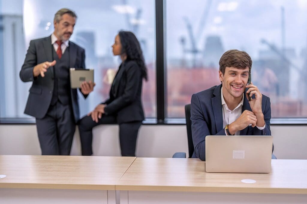 Business professionals engaged in IT discussions, one man on a phone, another with a tablet, in a modern office setting, emphasizing Reliable Networks' local IT support services.