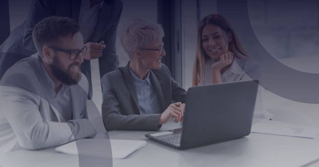 Group of professionals collaborating around a laptop, discussing strategies for Windows 10 migration and cybersecurity solutions.